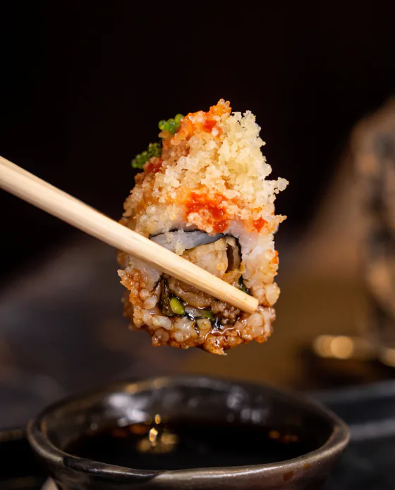 A piece of crunchy roll lifted with chopsticks over soy sauce