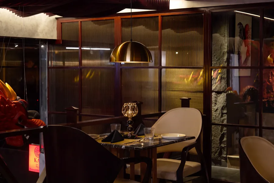 A table for two under a brass pendant at KAO, the dragon's head beside the balcony